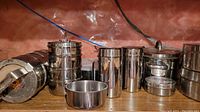 Shelving with multiple stainless steel containers, pots and plates arranged, showing reflective polished surfaces and different container sizes.