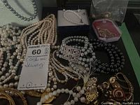 Several pearl and faux pearl necklaces, some gold-tone bracelets, and earrings on a dark surface.