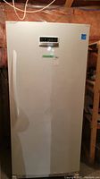 Front view of white upright freezer with door closed, showing digital control panel on upper center of door.