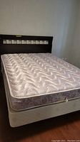 Full view of bed showing wooden headboard, mattress with floral pattern, and bed frame.