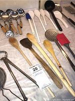 Kitchen utensils laid out on white table surface, showing the ladles, wooden spoons, spatulas, pestle and mortar, and other tools
