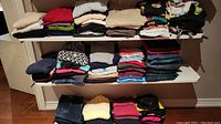 Three shelves of folded ladies clothing including sweaters, tops, and denim jeans in assorted colors and styles.