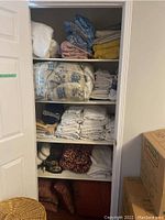 Closet with shelves holding folded assorted linens including sheets, towels, face cloths, blankets, and cushions.