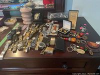 Wide view of watches, cufflinks, keychains, container, beads, and cardholder on dark surface