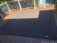 Full view of the large dark gray woven outdoor rug placed on deck floor.