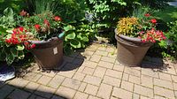 Two brown resin planters side by side on a brick patio with green foliage backdrop.