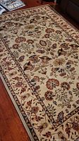 Full view of the cream floral area rug on wood floor near couch and table.