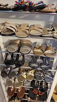Close-up of shoes on a metal shoe rack featuring beige, gold, black, and brown sandals and slip-ons.