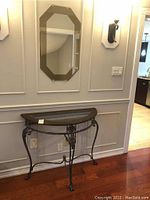 Photo showing the console table with metal frame, wood and glass top, and the octagonal beveled mirror mounted on wall above it.