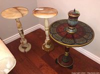 Photo of two stone pedestal tables and one decorative pedestal table with lidded jar on top, showing overall lot contents.