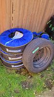 Four stacked tires covered with Michelin blue tire covers, next to one tire mounted on steel rim.