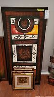 Four framed artworks stacked with two large vertical abstract art pieces on top and two smaller gold framed pieces leaning in front