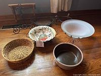 Overview of various bowls and stands placed on wooden floor including ceramic, glass, and wicker bowls alongside wooden shelf and metal stands.