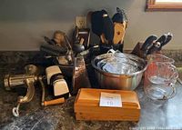 Photo showing various kitchen tools including a metal meat grinder, graters, shredders, mixing bowls, glass measuring cups, and a wooden cutlery box.