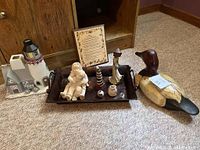 Overall display of lot items including metal tray with small decor items, sculpture of children, wood duck, lighthouse candle holder, and framed print.