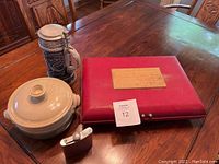 Six-piece silverplate flatware case, pottery dish with lid, Gerzit beer stein, and flask arranged on a wooden table