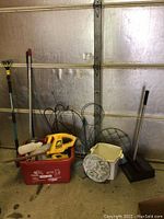 Full lot showing an assortment of gardening and cleaning tools plus garden wire in front of garage door