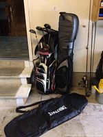 Photo of multiple golf clubs stored in a golf bag and two golf club travel bags placed beside it.