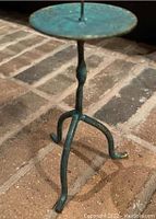 Metal tripod candle holder with rustic green patina on brick floor to show detail
