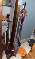 Photo of multiple floor cleaning tools including Hoover hard floor cleaner, Shark steam mop, Vileda mop, mop pads, bucket and cleaning sprays in corner area.