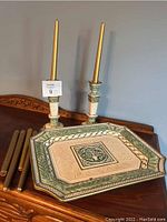 Set of two ceramic candle holders with tapered gold candles and a rectangular platter with embossed leaf and tree motif in green and beige tones.