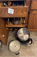 Pots, pans including large stainless steel stockpot and roasting pans on floor and in cabinet under kitchen counter.