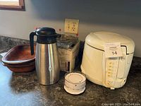 Shows a stainless steel thermal coffee carafe, wooden clay roaster bowl, boxed vegetable steamer, white hamburger press on a countertop.