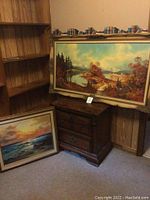 Photo showing wooden 2-drawer table with large framed scenic print on top and a smaller framed ocean print on floor.