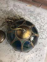 Photo of the hanging lamp's stained glass shade, showing blue and green glass panels with metal detailing and attached wires and chains.
