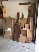 Photo showing drywall sheets stacked vertically along with varied wood pieces leaning against wall.