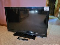 Front view of 42-inch Sceptre TV with black bezel sitting on a stand and remote control placed on the carpet in front of it.