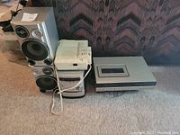 Two Sony stereo speakers, a Sony receiver, and a cassette deck arranged on carpeted floor.