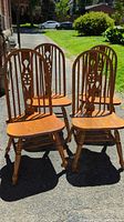 Four solid wood dining chairs arranged outdoors on pavement, showing front and side views with sunlight highlighting the wood grain.