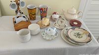 Full set of the tea and coffee items on a white tablecloth showing all cups, plates, teapot, and mugs