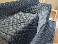 Blue quilted bedspread partially covering a sofa and spread on floor