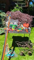 Full view of garden tools on table with extension pole leaning, garden arch on grass below