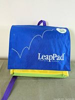 Closed LeapPad fabric carrying case is blue with green and yellow accents and a purple strap. Shows branding on the front flap.