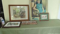 Photo showing all items on green tablecloth: framed chipmunk print, bathroom sign, framed Westdale Village print lying flat, Chinese movie poster on a black board, and small framed cartoon.