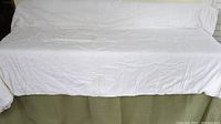 Full view of the white silk duvet spread out on a green couch, showing its size and texture.
