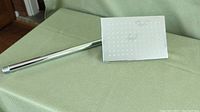 Top-down view of the rectangular chrome showerhead and its long attached pipe resting on a green surface.