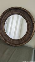 Front view of the round mirror showing ornate bronze frame and reflective glass.