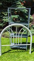 Photo showing the white metal shelving unit with the white metal single bed headboard leaning against it, outdoors on grass.