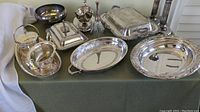 Image showing various silver plate pieces arranged on a green tablecloth, including bowls, covered dishes, and trays.