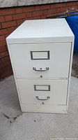 Front view of a two drawer metal file cabinet with handles and label slots on each drawer.