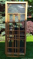 Photo showing one of the two wooden framed 32x80 screen doors with mesh screen and decorative window inserts leaning against an outdoor background.