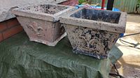 Pair of square vintage cement planters showing front and side views, placed on a green tarp outdoors.