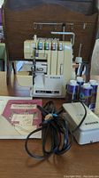 Vintage beige Singer Ultralock 14U64A serger with power cord, foot pedal, and thread cones on a wooden table.