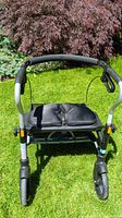 Front view of Evolution Xpresso Lite Mini walker showing padded black seat, ergonomic handles, and front wheels, placed on grass outdoors.