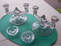 Two Waterford crystal ring holders, clear glass, each with a single prong center, sitting on etched smoky glass candelabra bases placed on a green mat outdoors.