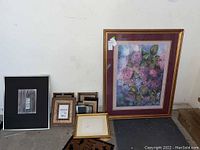 Overview of lot showing large framed hydrangea print leaning against wall with smaller picture frames stacked nearby on floor